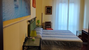 Habitación de hotel con cama, escritorio, silla, lámpara, marco de foto y un cuadro en la pared.