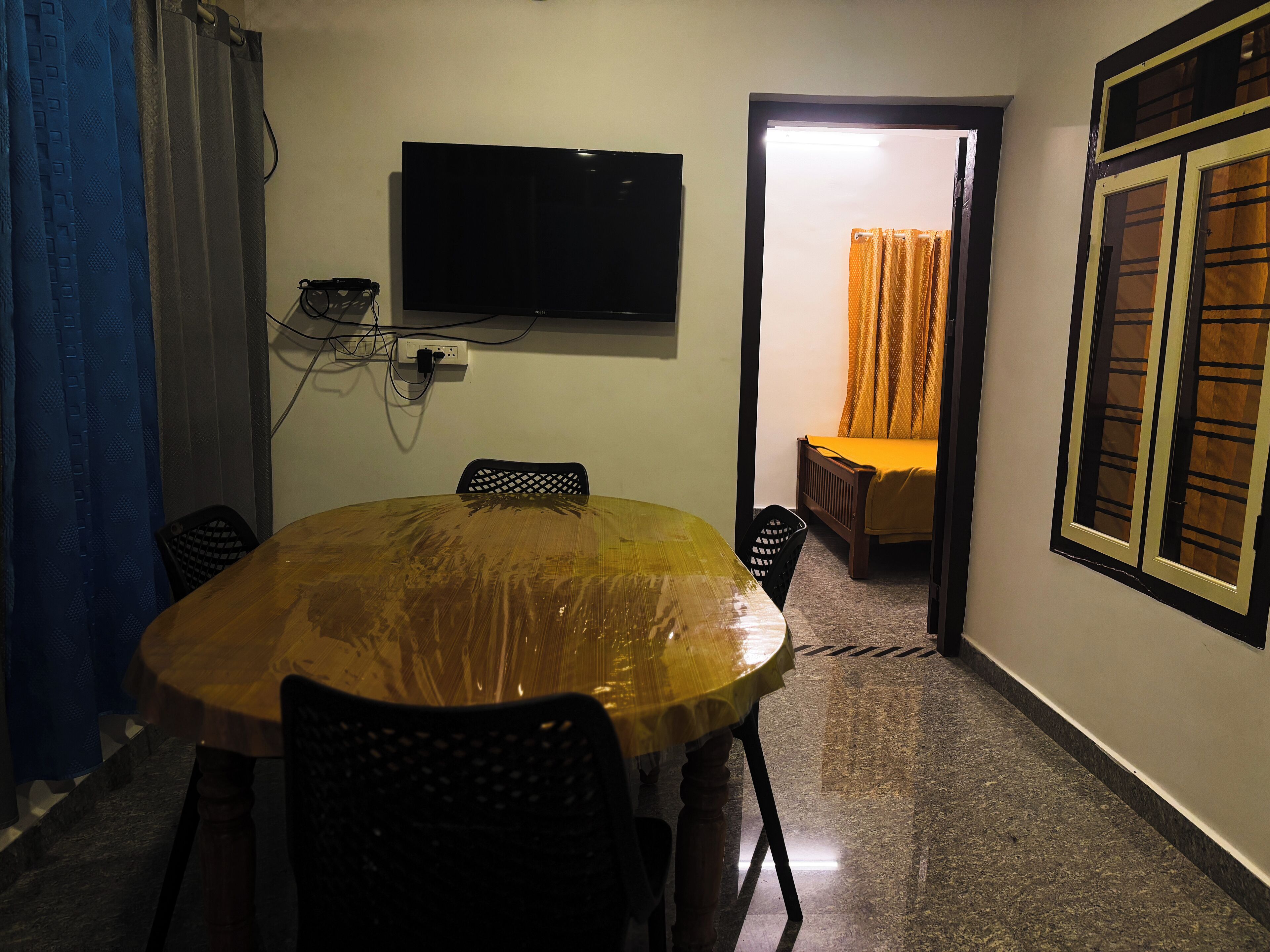 Ein Zimmer mit einem runden Holztisch, Stühlen, einem an der Wand montierten Fernseher und einem Bett mit orangefarbener Bettdecke.