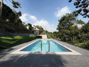 A rectangular swimming pool with a tiled edge, surrounded by a paved deck.
