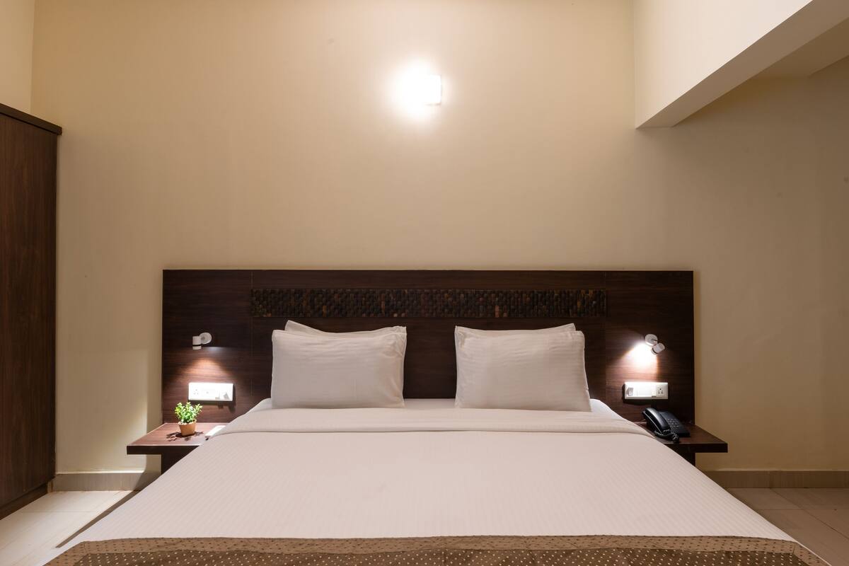 A hotel room with a large bed, two bedside tables with lamps, a wooden wardrobe, and a small potted plant.