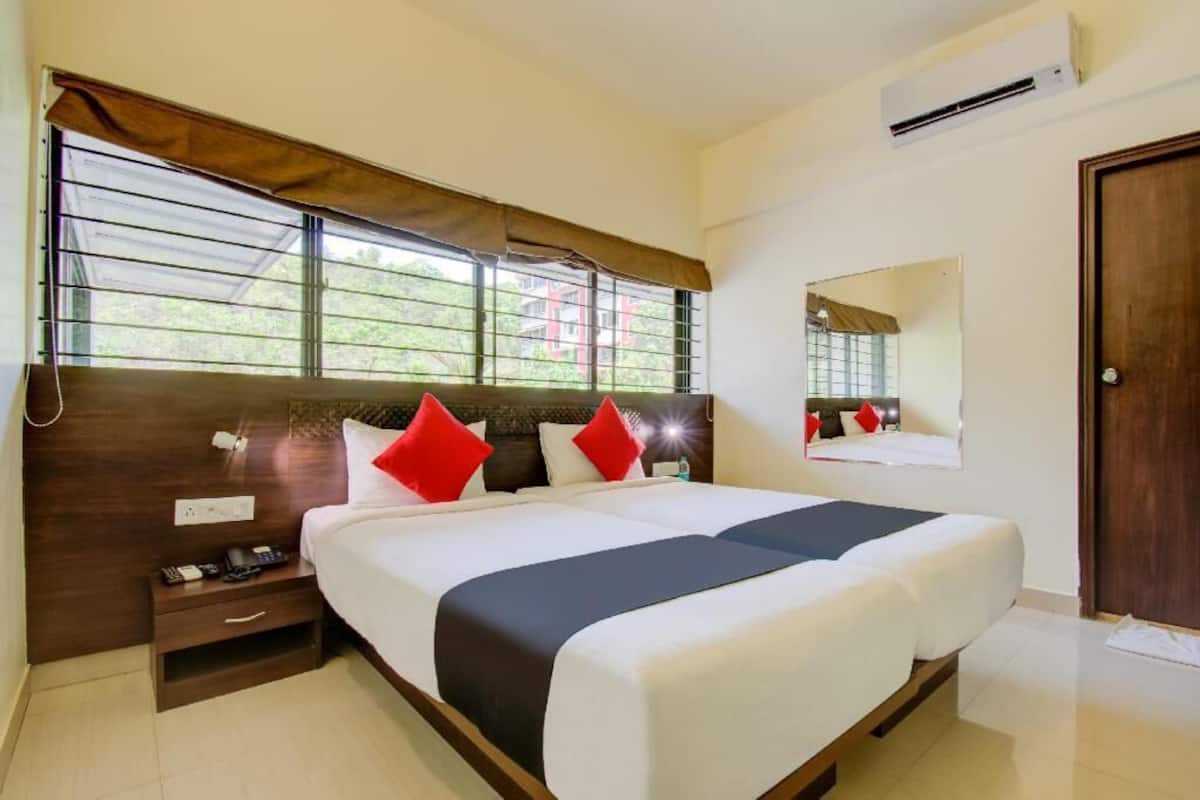 A hotel room with a large bed, a nightstand, a mirror, and an air conditioning unit.