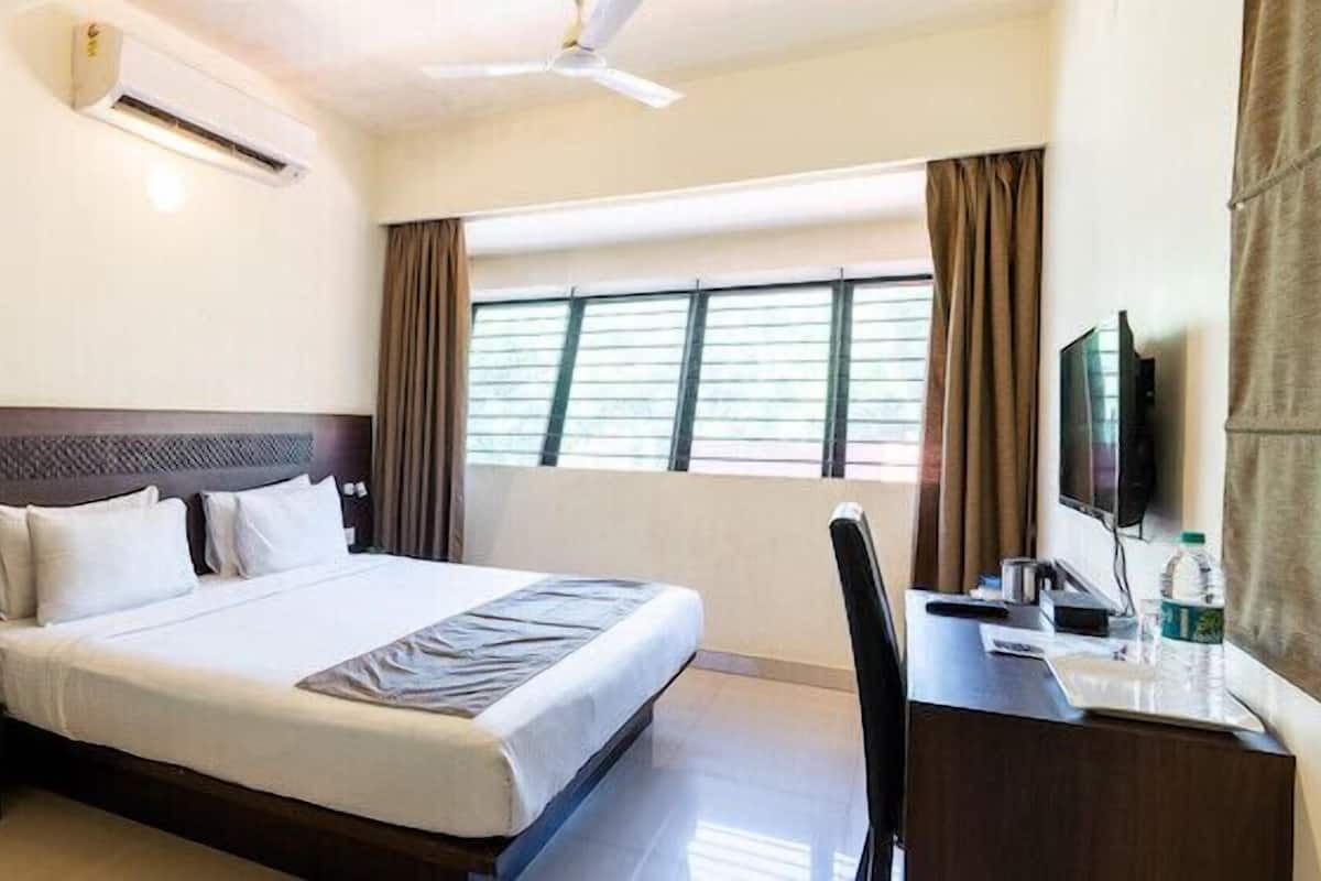 A hotel room with a bed, a desk, a chair, a television, and an air conditioning unit.