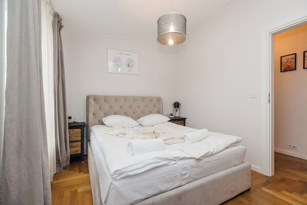 Un lit bien fait, avec du linge de lit blanc, une tête de lit et une table de chevet sur laquelle se trouve une lampe.