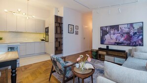 Una sala de estar moderna con un sofá, una mesa de centro con flores, un televisor y una zona de cocina con armarios y una mesa de comedor.