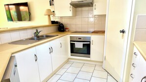 Een compacte keuken met witte kastjes, een inbouwoven, een magnetron en een spoelbak.