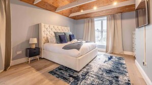 A bedroom with a large bed, a nightstand, a TV, and a view of the outside.