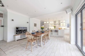 A modern kitchen with white cabinetry, a dining area with wooden chairs, and a large window.