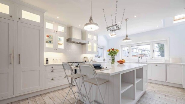 A modern kitchen with white cabinetry, a central island, bar stools, pendant lighting, and a view of the outside.