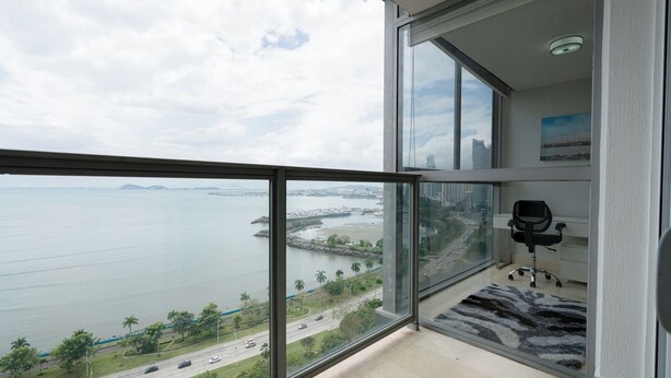 Un apartamento moderno en un edificio alto, con un balcón grande, vistas a la ciudad y un espacio de trabajo bien equipado.