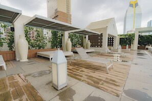 An outdoor lounge area with sun loungers, a large planter, and a pergola structure.