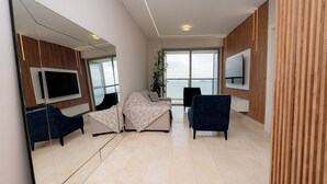 Habitación de hotel moderna con un espejo grande, dos sofás, un televisor y vista al mar.