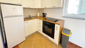 A compact kitchen with white cabinets, a built-in oven, a sink, and a window with blinds.