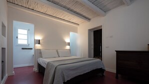 Un dormitorio con cama, lámparas de noche, cómoda y una puerta que da a otra habitación.