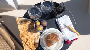 Una mesa redonda con una bandeja negra que contiene pan plano, un tazón de higos, dos vasos de agua, una botella y una servilleta envuelta.