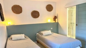 A room with two single beds, a wall-mounted light fixture, and a door leading to a bathroom. - Charming 18th-Century Townhouse with Private Terrace & Pool (Saint-Rémy-de-Provence)