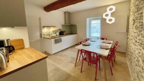 A compact kitchen with a wooden countertop, a dining area with red chairs, and a stone wall. - Charming 18th-Century Townhouse with Private Terrace & Pool (Saint-Rémy-de-Provence)