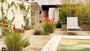 A pool area with a white chair, surrounded by plants and a stone wall. - Charming 18th-Century Townhouse with Private Terrace & Pool (Saint-Rémy-de-Provence)