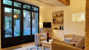 A living room with a sofa, armchairs, a coffee table, a TV, and a bookshelf. - Charming 18th-Century Townhouse with Private Terrace & Pool (Saint-Rémy-de-Provence)