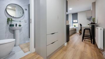 A modern bathroom with a toilet, sink, and mirror. There is a wooden floor and a small stool.