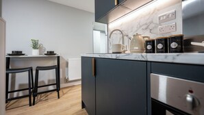 A modern kitchen with dark cabinetry, a marble countertop, a kettle, and a coffee maker. - Student Only Clyde Court (Glasgow)