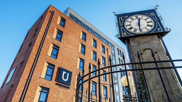 A tall brick building with a clock tower, featuring a prominent 'U' logo on the side. - Student Only Clyde Court (Glasgow)