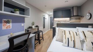 A modern hotel room with a bed, a desk with a chair, a small kitchenette, and a bathroom. - Student Only Clyde Court (Glasgow)