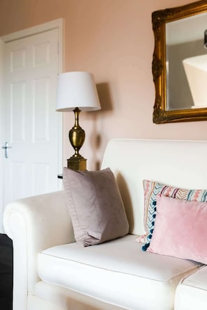 A white sofa with a gold lamp, a mirror, and a door in the background.