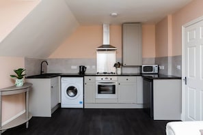 A compact kitchen with a washing machine, oven, microwave, and a small sink.