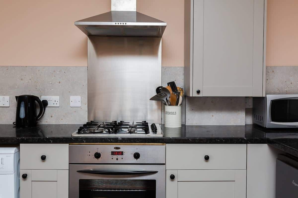 A kitchen with a gas stove, oven, stainless steel range hood, white cabinets, and a microwave.