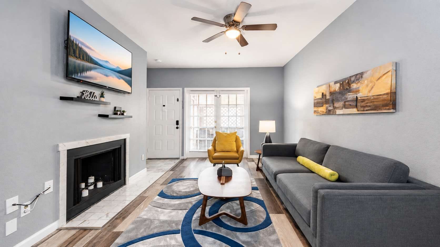 A living room with a fireplace, a sofa, a yellow armchair, a television, and a ceiling fan.