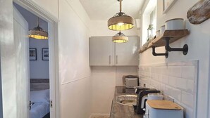 Una cocina estrecha con encimera de madera, dos lámparas colgantes, horno integrado y microondas.
