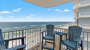 A balcony with two Adirondack chairs and a table overlooking a beach with a view of the ocean. - Coastal Hideaway: Cozy Beachfront Studio Sleeps 4 With Stunning Views! (Panama City Beach)