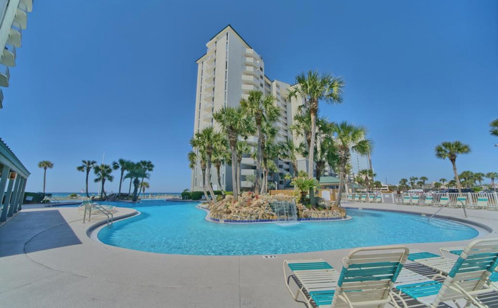 A pool area with lounge chairs, palm trees, and a tall building in the background.