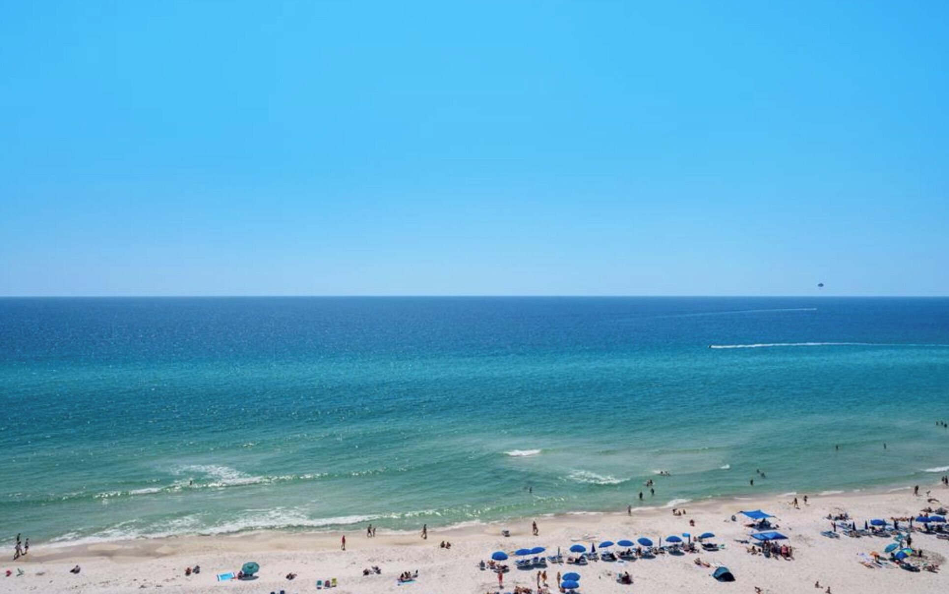 A beach with clear skies, calm waters, and numerous umbrellas.