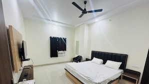 A hotel room with a bed, a desk with a computer, a TV, a ceiling fan, and a window with curtains. - HOTEL RAJDEEP (Sehore)