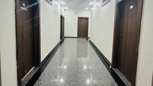 A hallway with a polished granite floor, wooden doors, and recessed ceiling lighting. - HOTEL RAJDEEP (Sehore)
