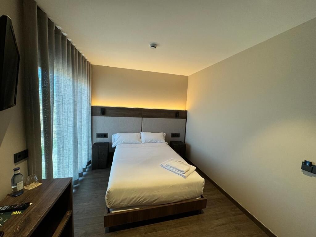 A hotel room with a bed, bedside table, and a nightstand.