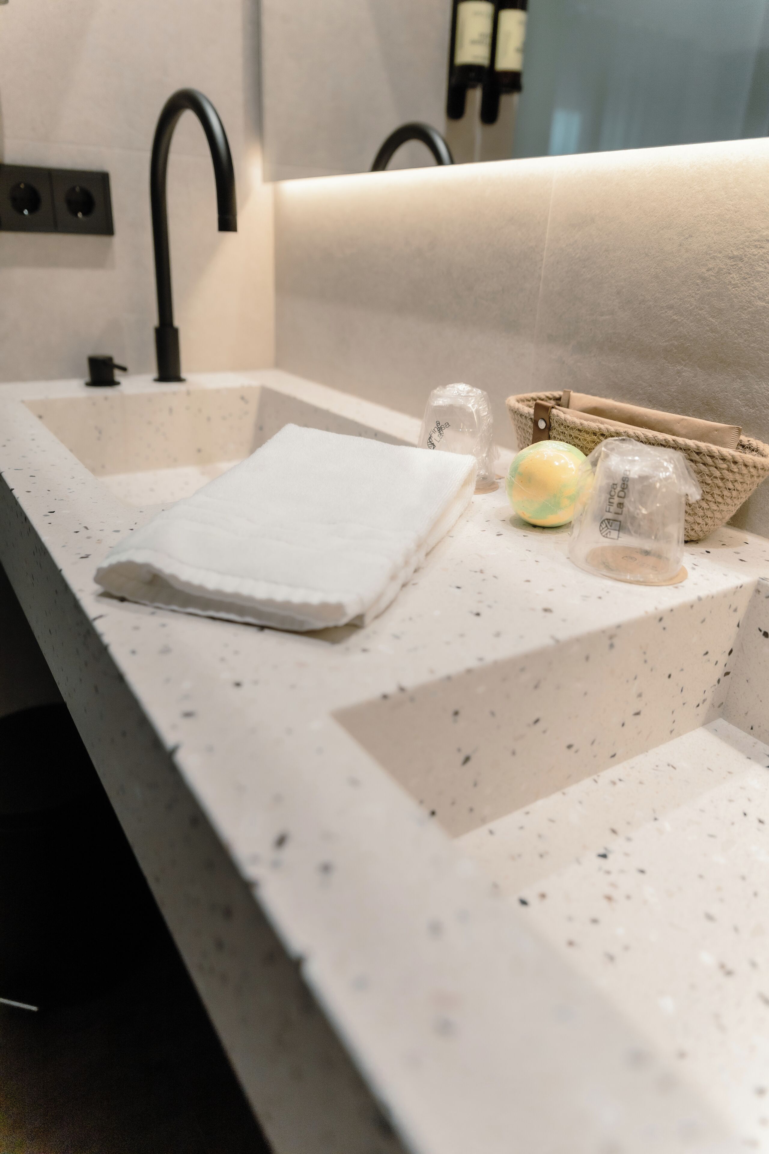 A bathroom sink with a white speckled countertop, a black faucet, and a beige woven basket with a white towel and a soap dispenser.