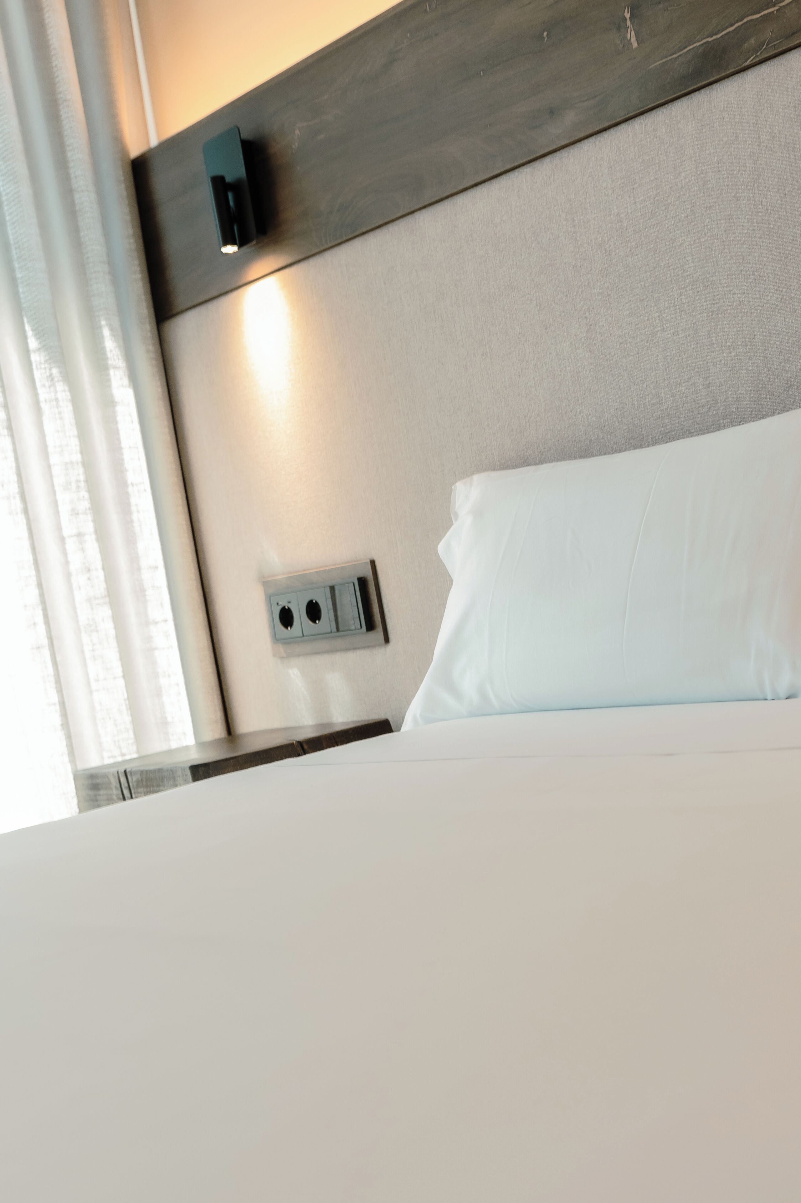 A hotel room with a bed, a wall-mounted light, and a power outlet.