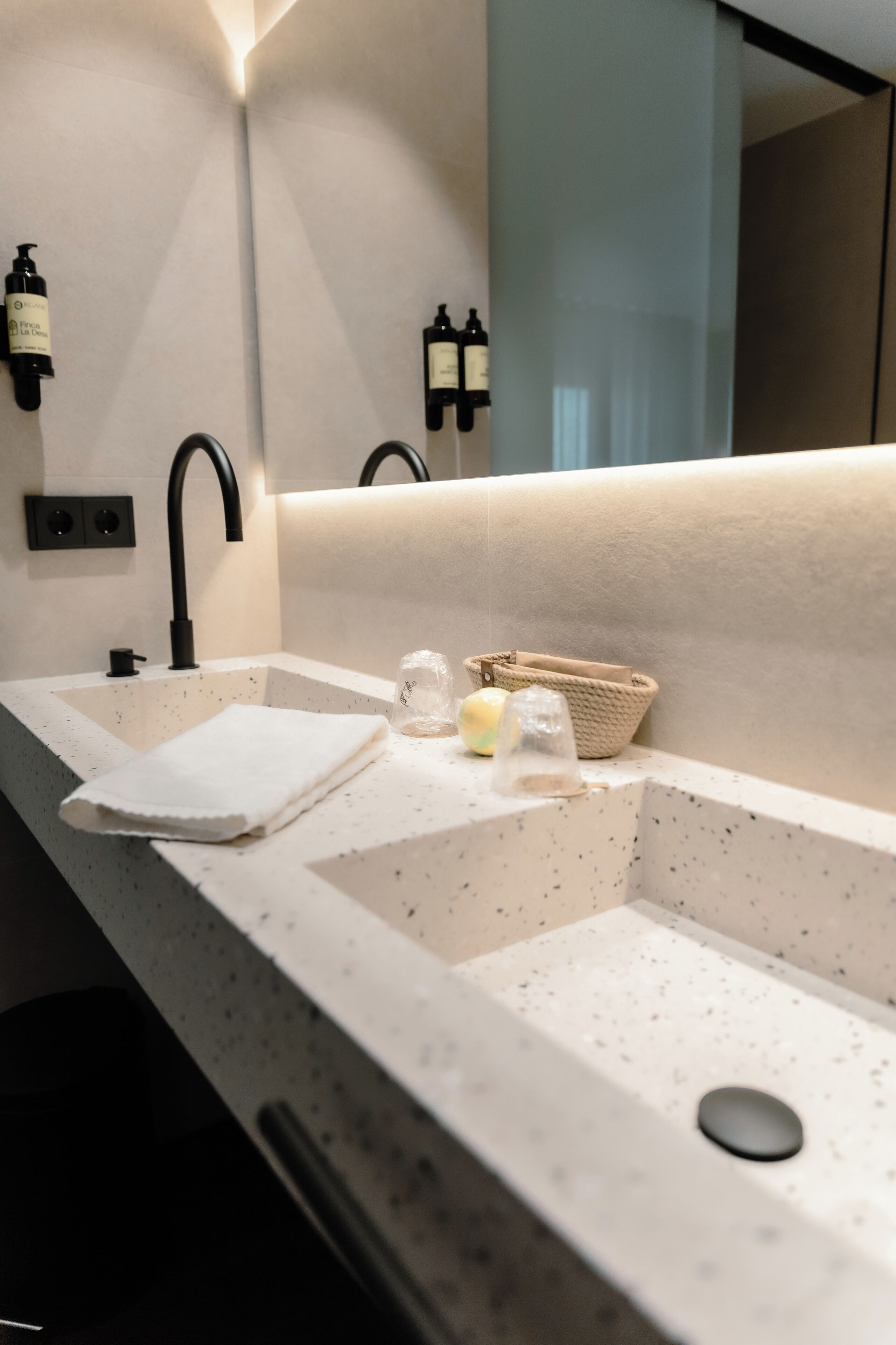 Ein Badezimmer mit einem weißpunktierten Waschbecken, einem schwarzen Wasserhahn, einem Handtuch, einem Glasbehälter und einem Korb.