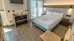 Une chambre d’hôtel moderne dotée d’un grand lit, d’un téléviseur à écran plat, d’un bureau avec un téléphone et une petite table, et offrant une vue sur la ville grâce à de grandes fenêtres.