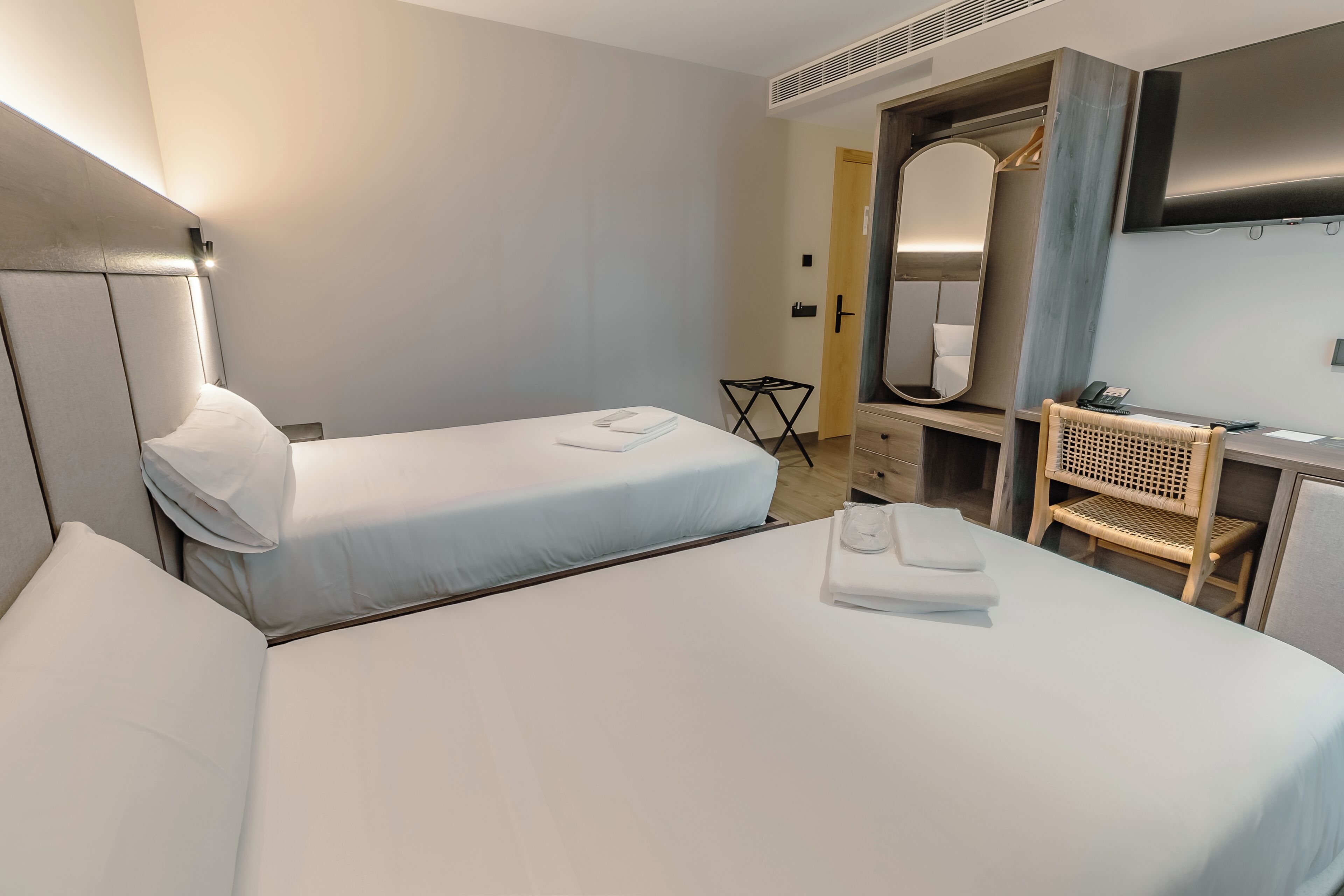 Een hotelkamer met twee bedden, een bureau, een stoel, een spiegel en een televisie.