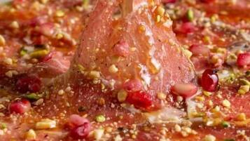 A plate of food with a fork lifting a piece of meat, garnished with nuts and pomegranate seeds.