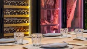 Un coin repas avec une table en bois dressée pour quatre personnes, un meuble à vin contenant des bouteilles et un présentoir à viande.