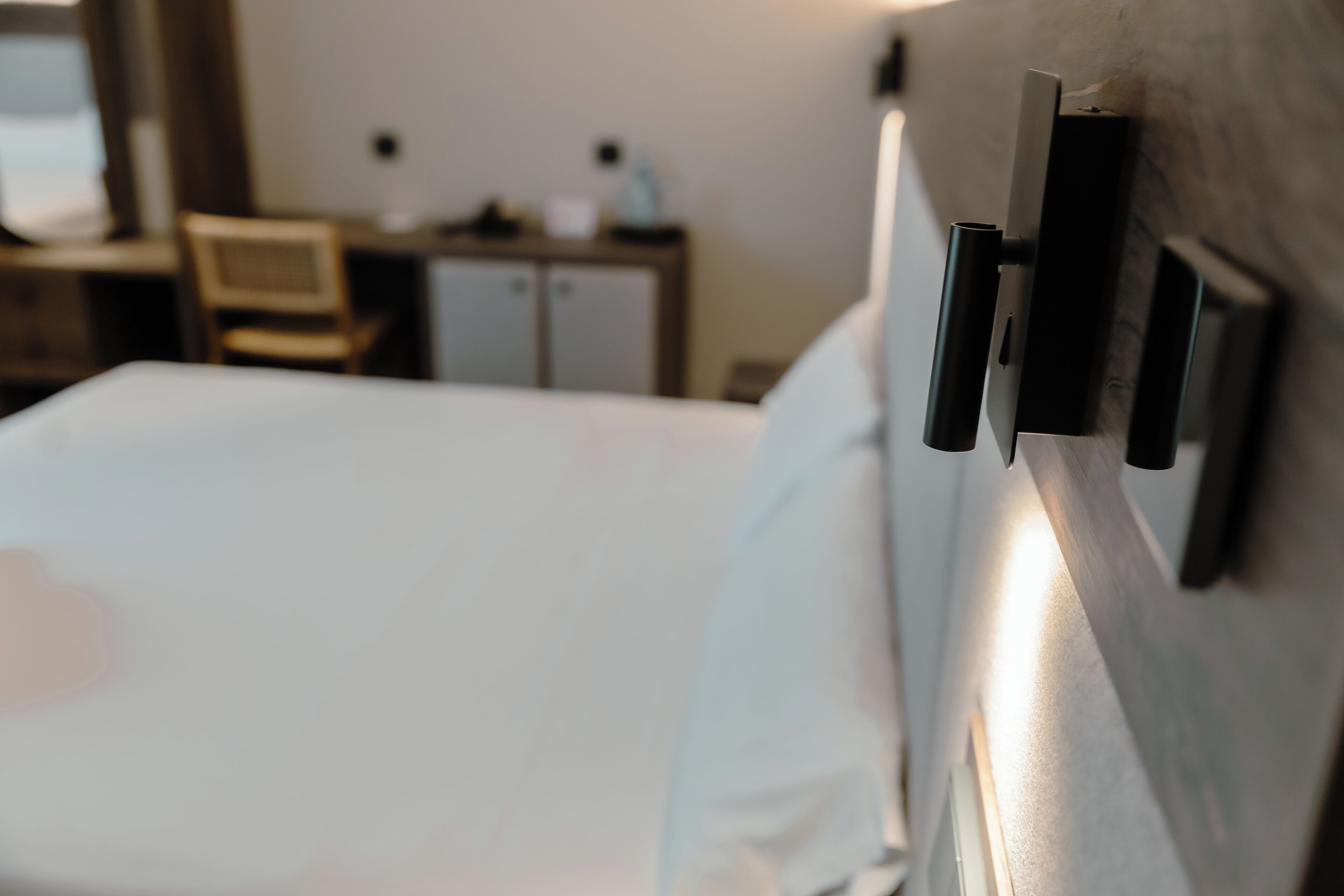 Ein Hotelzimmer mit einem ordentlich bezogenen Bett, einem hölzernen Kopfteil und einem Schreibtisch mit Stuhl im Hintergrund.