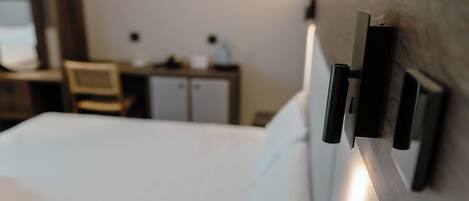 Ein Hotelzimmer mit einem ordentlich bezogenen Bett, einem hölzernen Kopfteil und einem Schreibtisch mit Stuhl im Hintergrund.