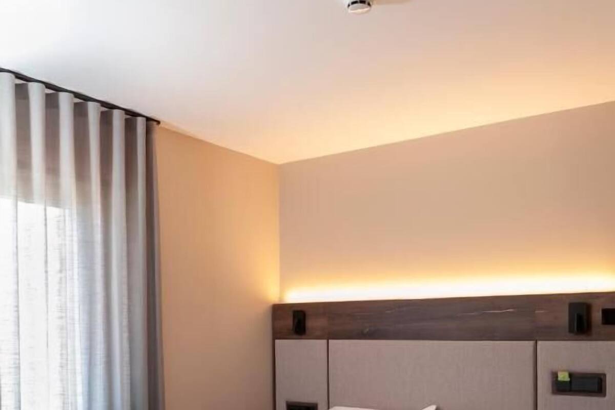 A modern hotel room with a large bed, wooden headboard, and a bedside table.