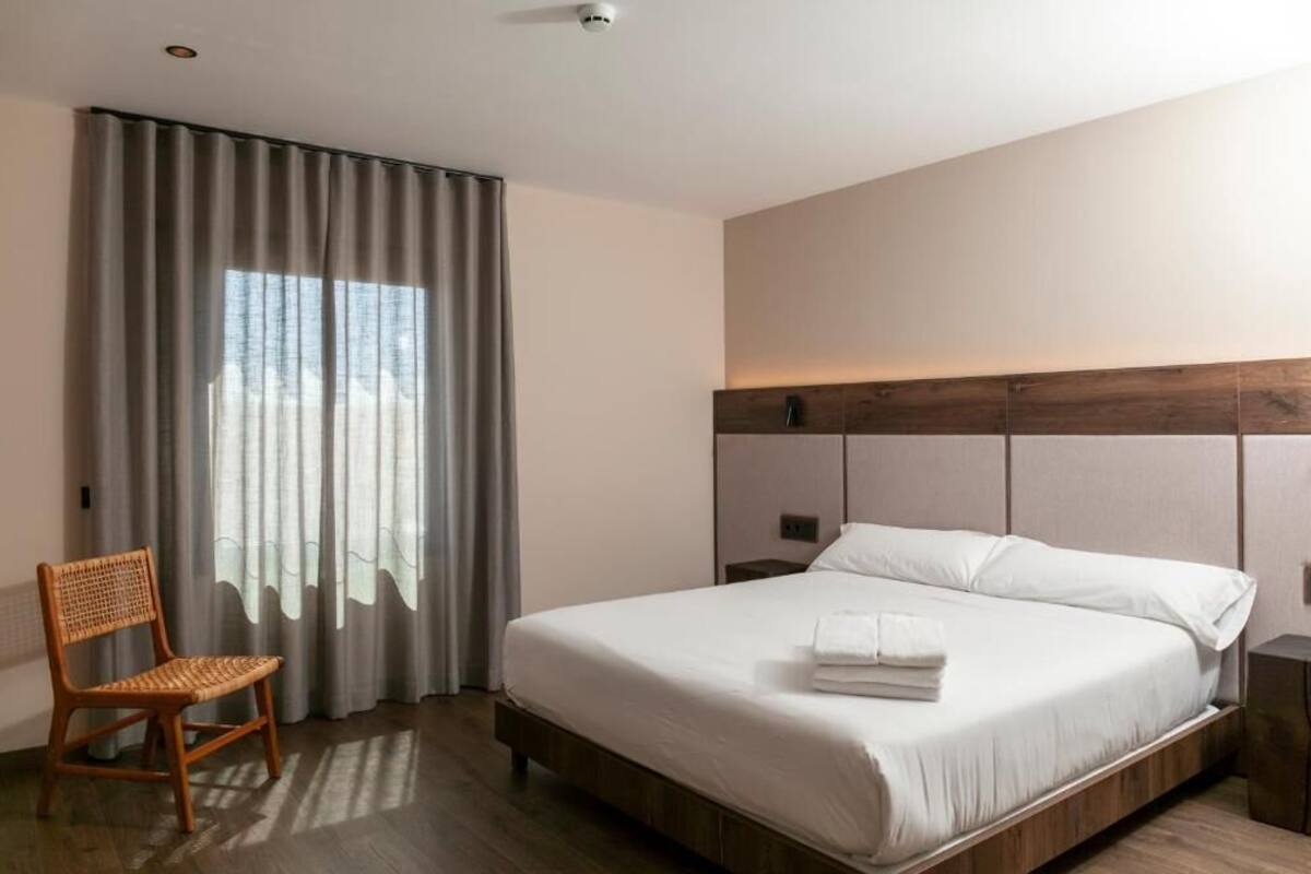 A hotel room with a large bed, a wooden headboard, a chair, and a window with curtains.