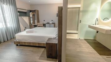 Ein modernes Hotelzimmer mit einem großen Bett, einem Nachttisch aus Holz, einem Schminktisch mit Spiegel und einer Duschkabine.