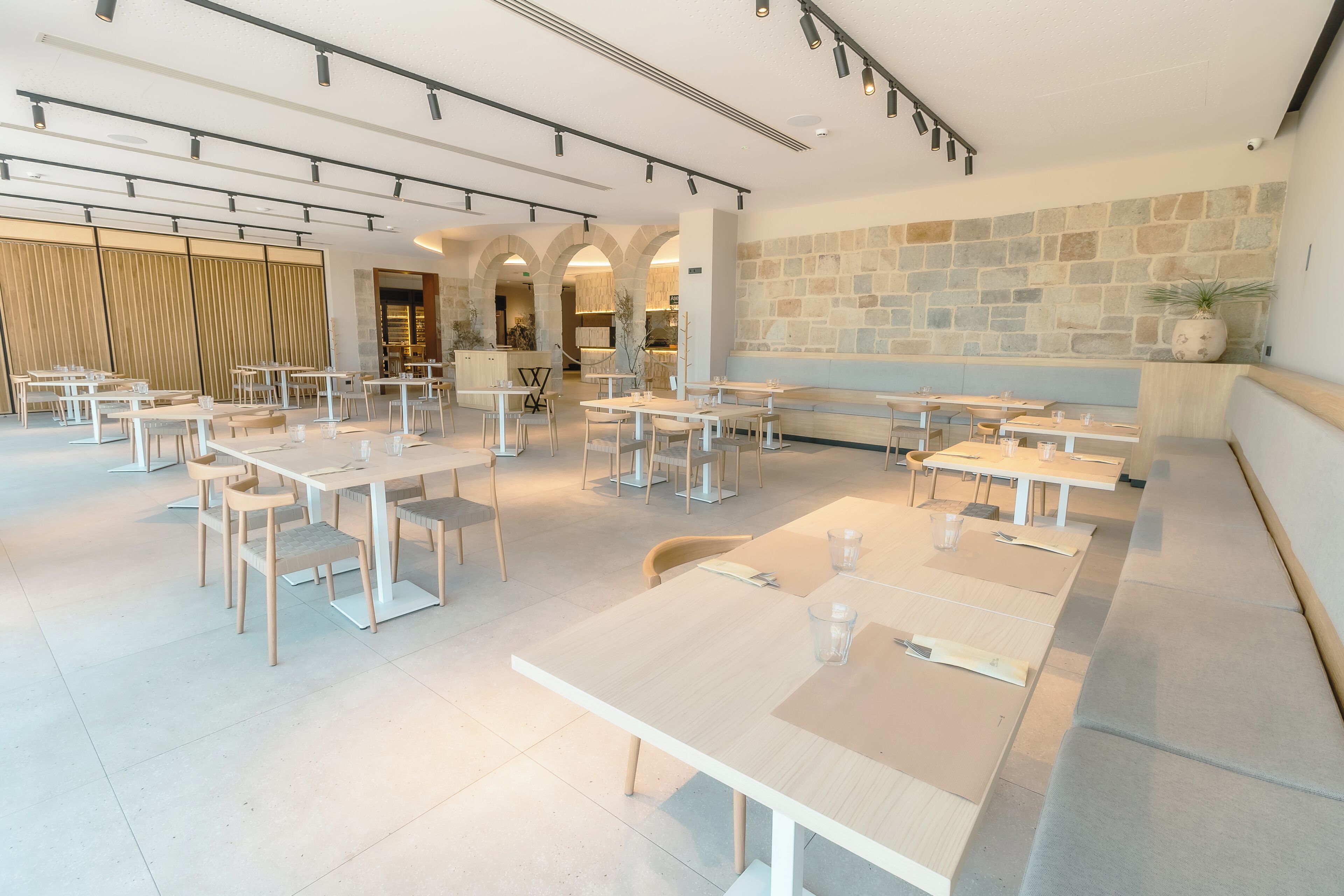 Un comedor amplio con varias mesas y sillas, una pared de piedra y un diseño moderno de techo.